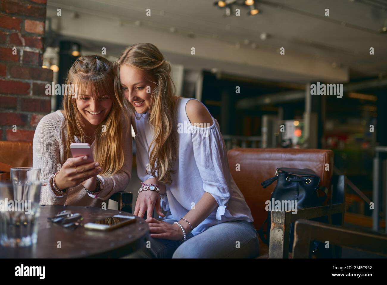 Wait, lemme show you. two attractive young girlfriends looking at a cellphone while sitting in a cafe. Stock Photo