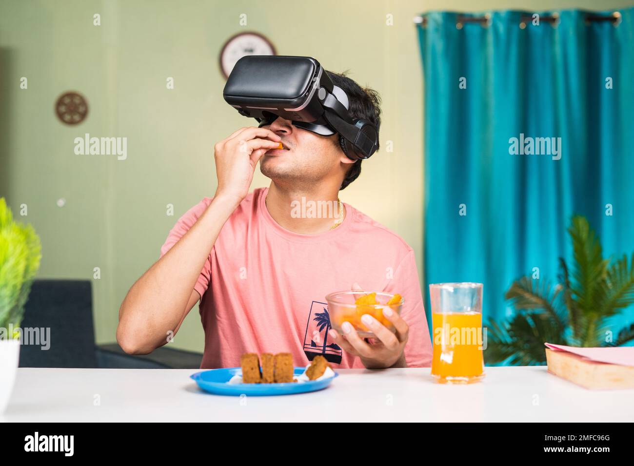addicted Young man with VR or virtual reality having snacks on metaverse while sitting at home - concept of futuristic, modern lifestyle and Stock Photo