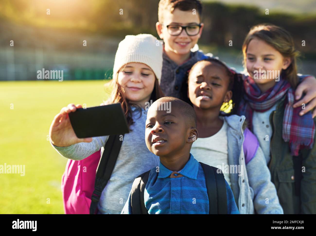 Everyone gather around for the picture guys. a group of elementary school kids taking a selfie together on the school lawn outside. Stock Photo