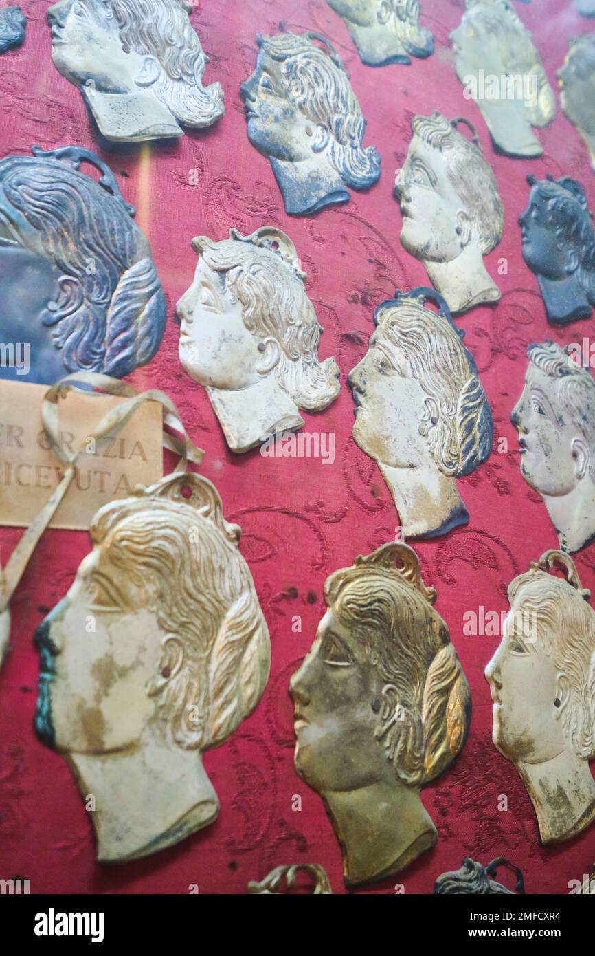 A wall of mounted votive offerings of tin, bronze, flat images of heads in profile. At the Chiesa del Gesù Nuovo Catholic church in Naples, Napoli, It Stock Photo