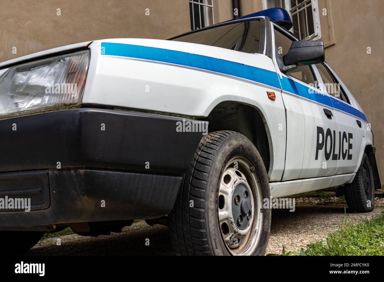 An old police car stands in front of a building with barred windows Stock Photo