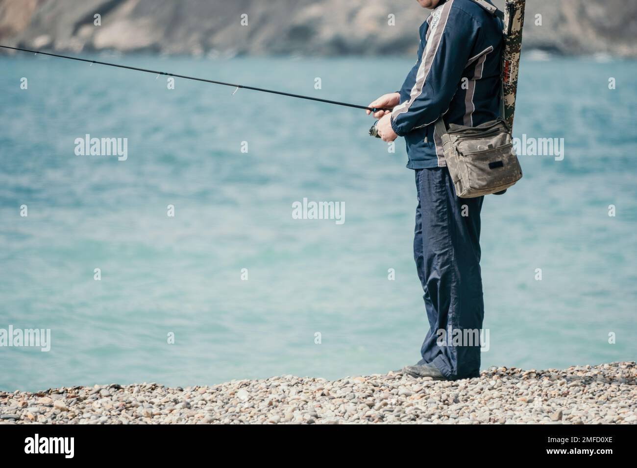 Man hobby fishing on sea tightens a fishing line reel of fish summer. Calm surface sea. Close-up of a fisherman hands twist reel with fishing line on Stock Photo