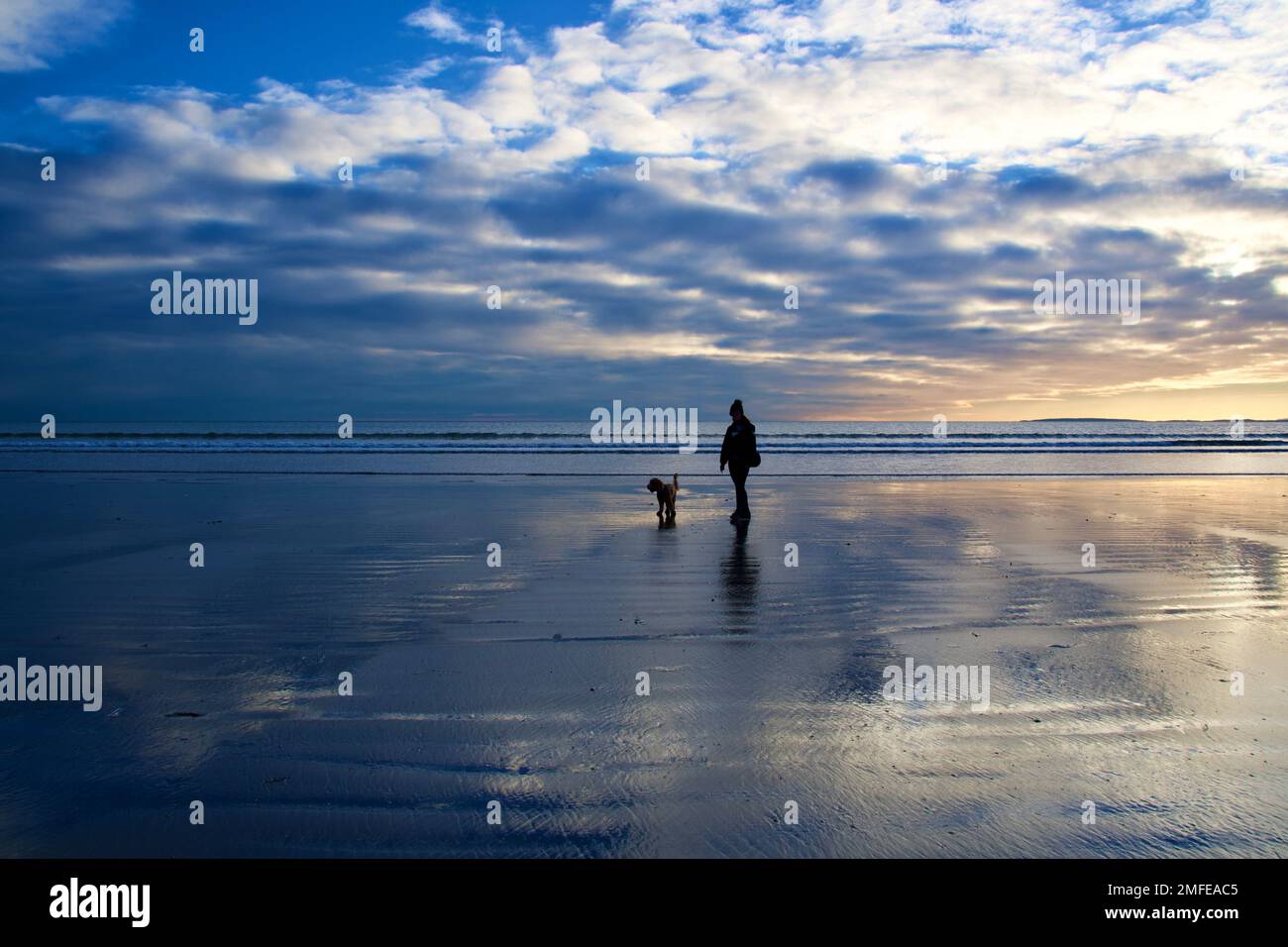 wintery sunset beach scene with a lone dog walker Stock Photo