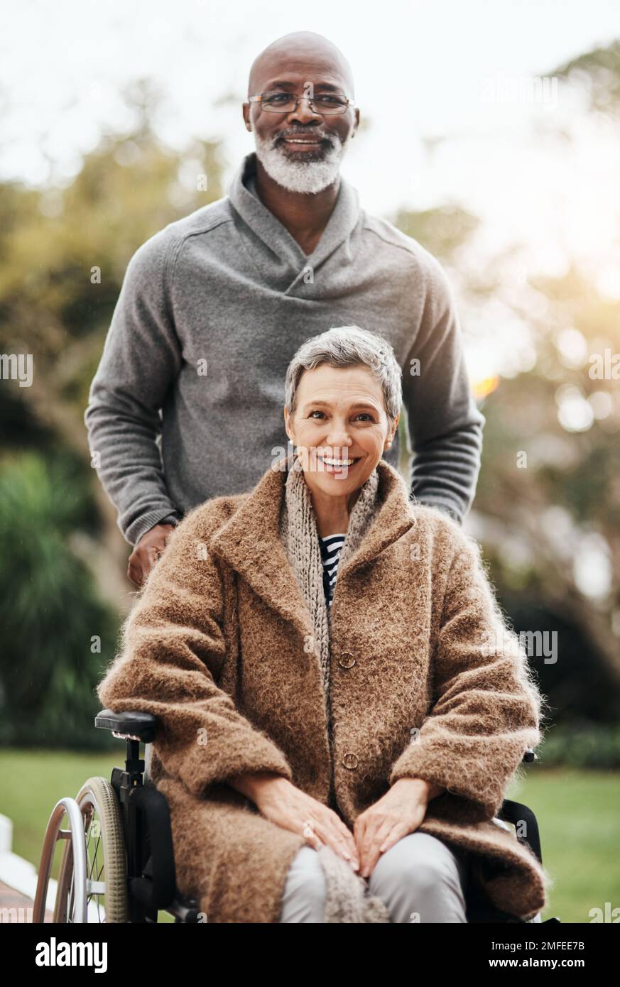 Hes still got her back after all these years. an elderly man pushing his wife in her wheelchair outside their home. Stock Photo