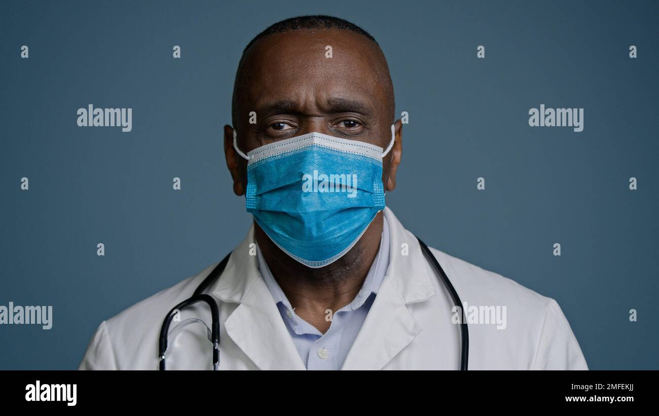 Serious african american mature man doctor surgeon therapist in medical gown and protective mask looking at camera posing in studio gray background Stock Photo