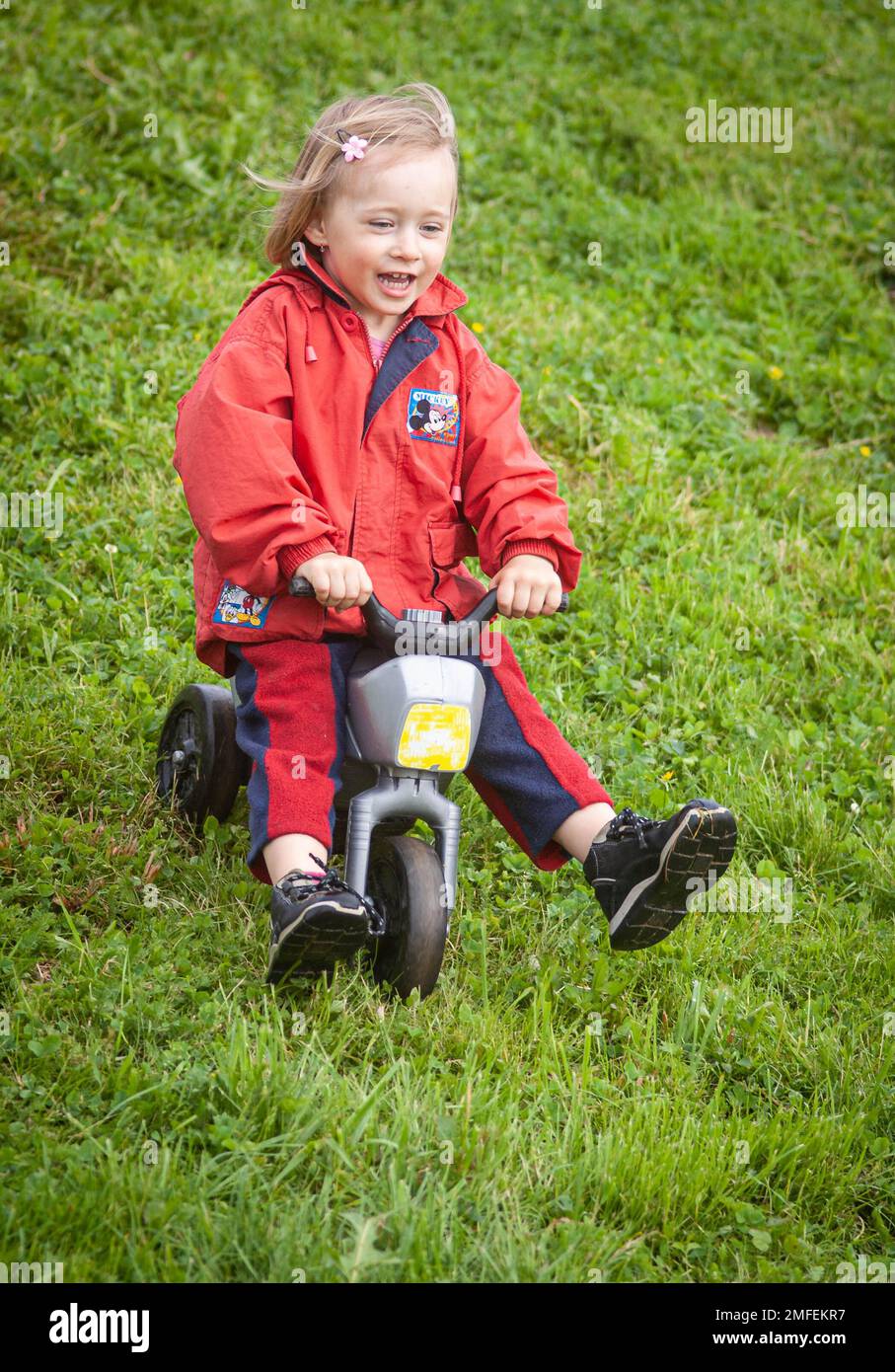 A smiling baby girl enjoying riding a push bike downhill Stock Photo