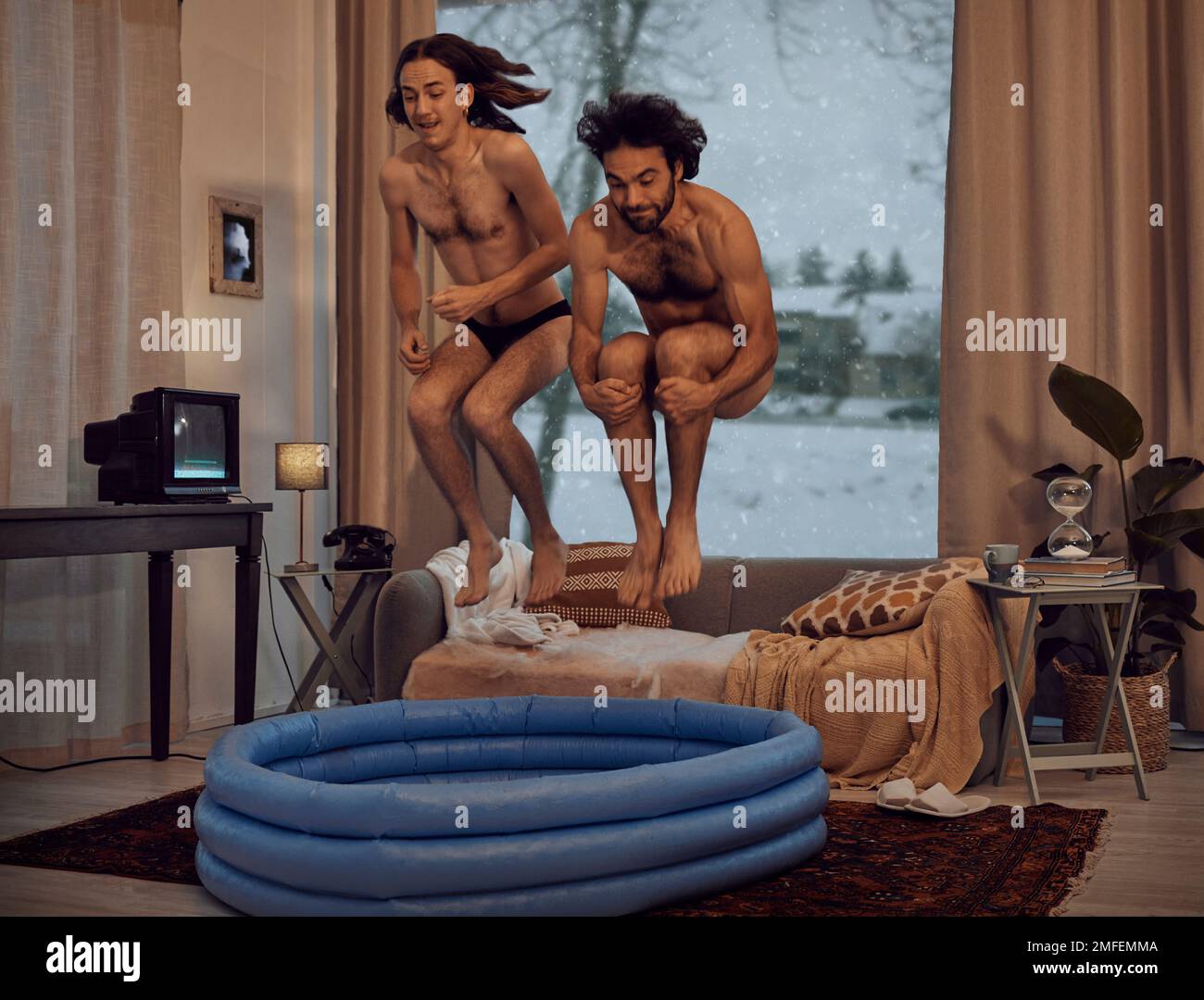 Hipster, rebel and jump into inflatable pool in a lounge inside a retro home or house having fun and playing. Funny, snow and men dive together in the Stock Photo