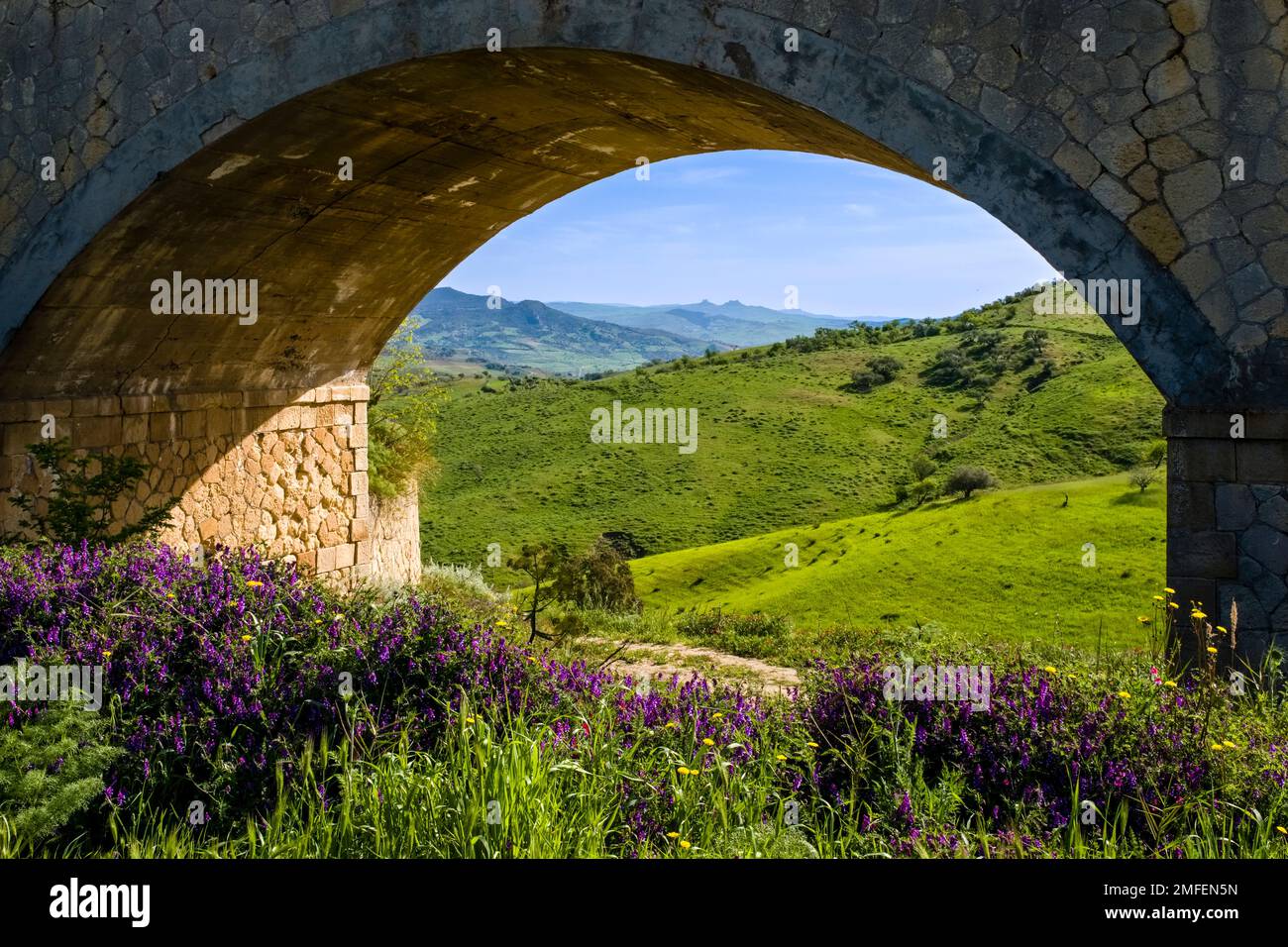 Agricultural landscape with green hills, trees and fields in Central Sicily, seen through the arch of a bridge. Stock Photo