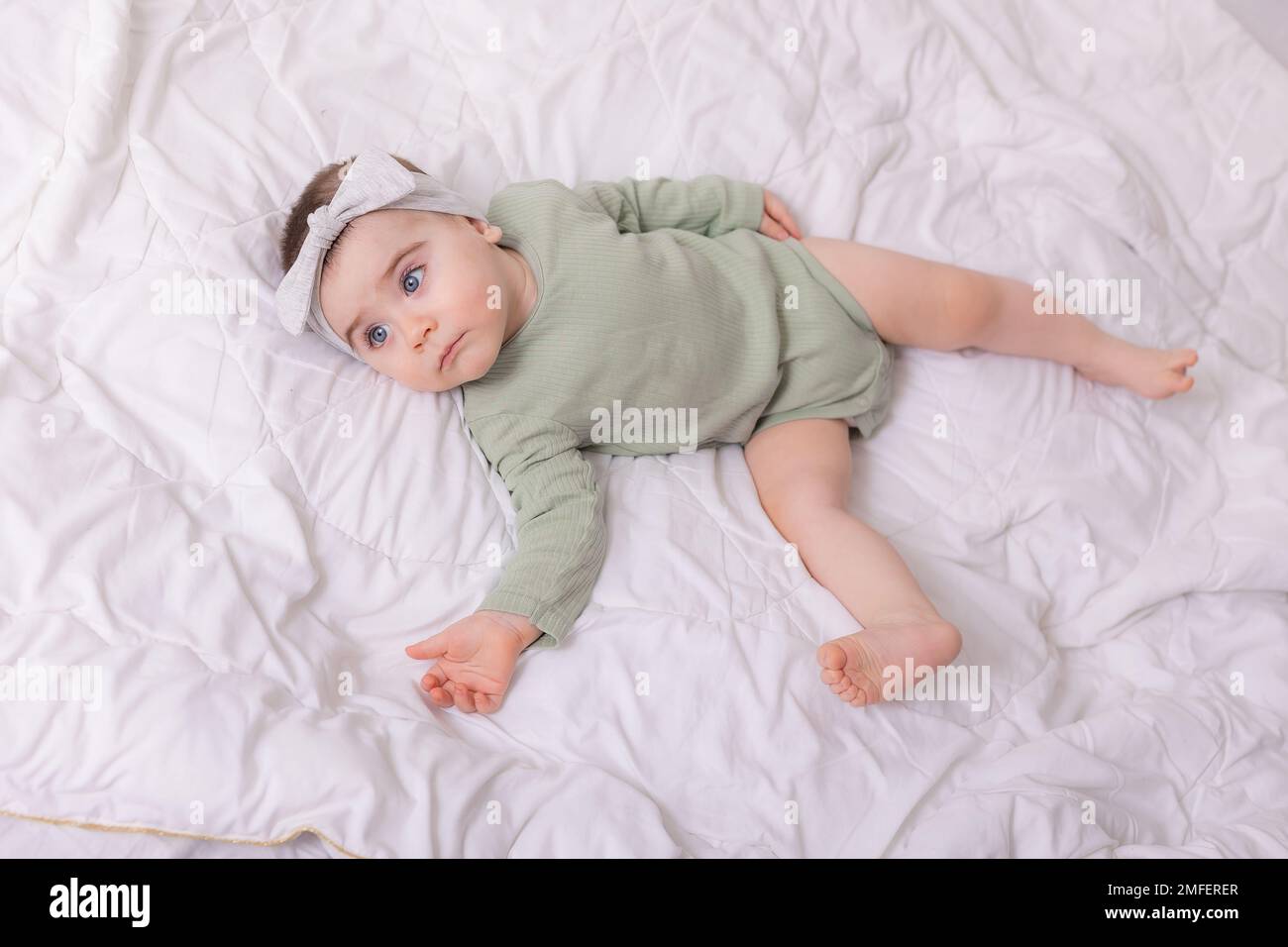 a girl with beautiful big eyes is rubbing the baby at home on the bed in a cotton bodysuit on white bed linen. High quality photo Stock Photo