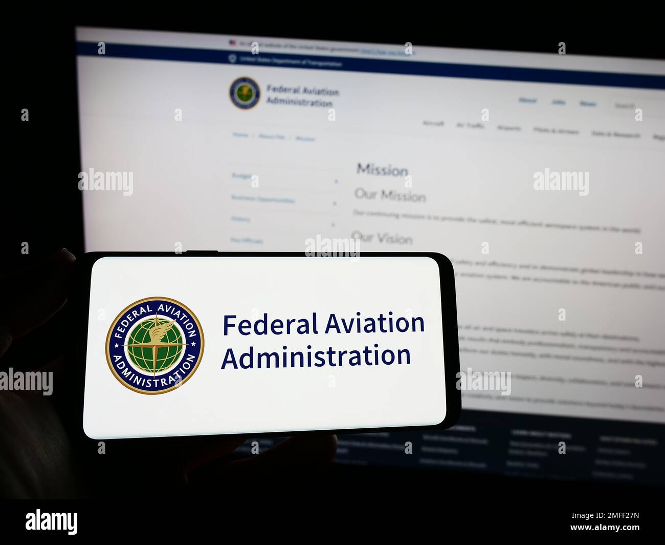 Person holding smartphone with seal of US Federal Aviation Administration (FAA) on screen in front of website. Focus on phone display. Stock Photo