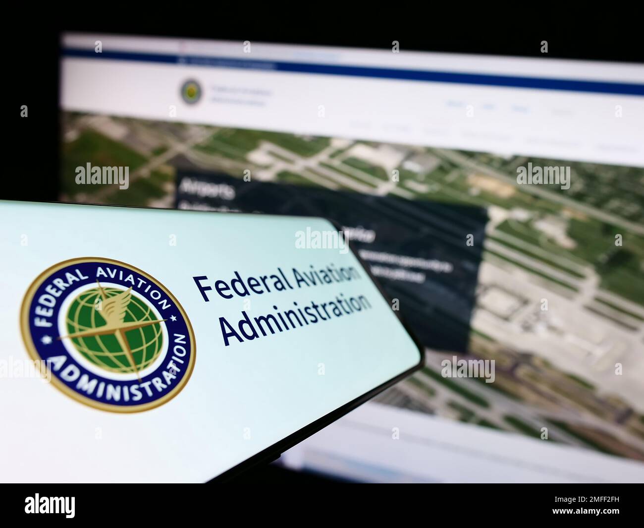 Cellphone with seal of US Federal Aviation Administration (FAA) on screen in front of website. Focus on center-left of phone display. Stock Photo