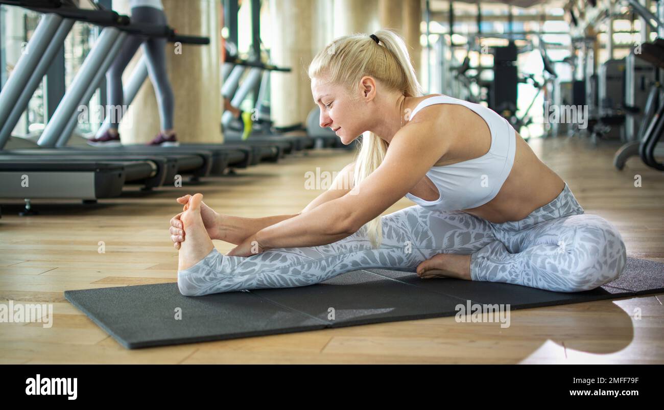Fitness blonde haired woman stretching on exercise mat at gym Stock ...