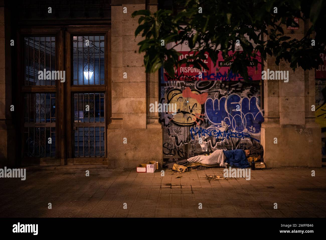 A homeless man sleeps on the sidewalk in downtown Barcelona, Spain ...