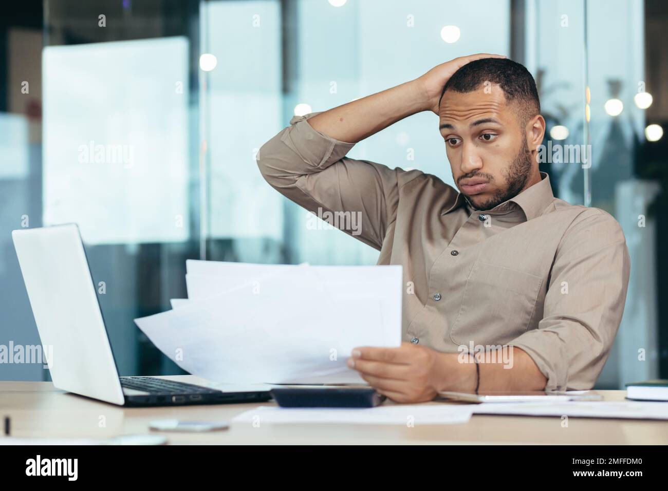 Worried young African American male student holding papers in hands. I received a letter, bad exam results, refusal of admission. Upset, holding his head. Stock Photo
