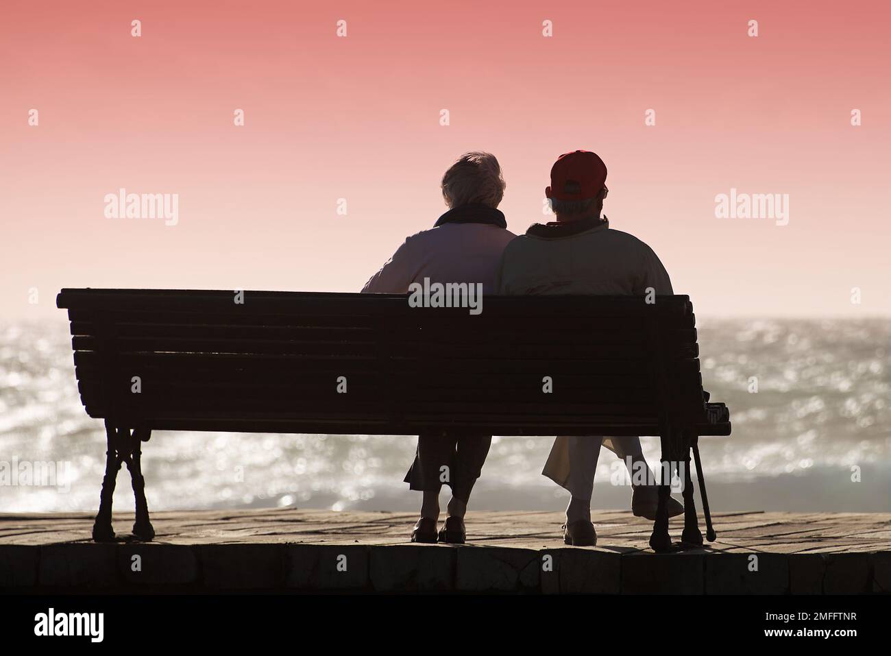 Silhouette seniors couple waiting for colourfull sunset on the bench near ocean Stock Photo