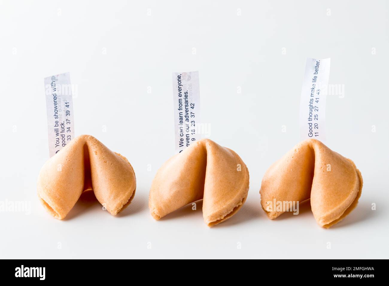 Three crispy fortune cookies in a row with fortune notes inserted. Stock Photo