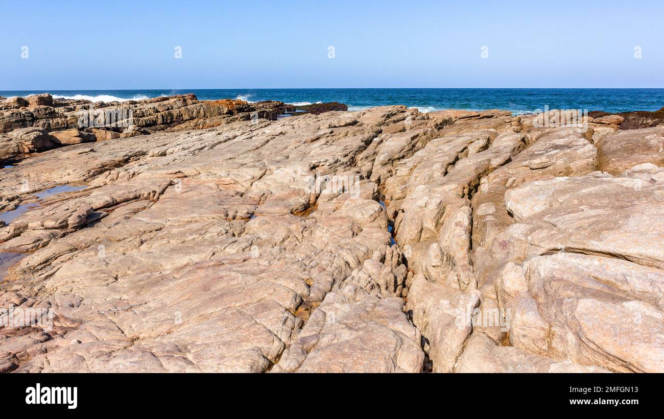 Ocean rocky beach coastline rock shelf ledge into blue calm sea waters. Stock Photo