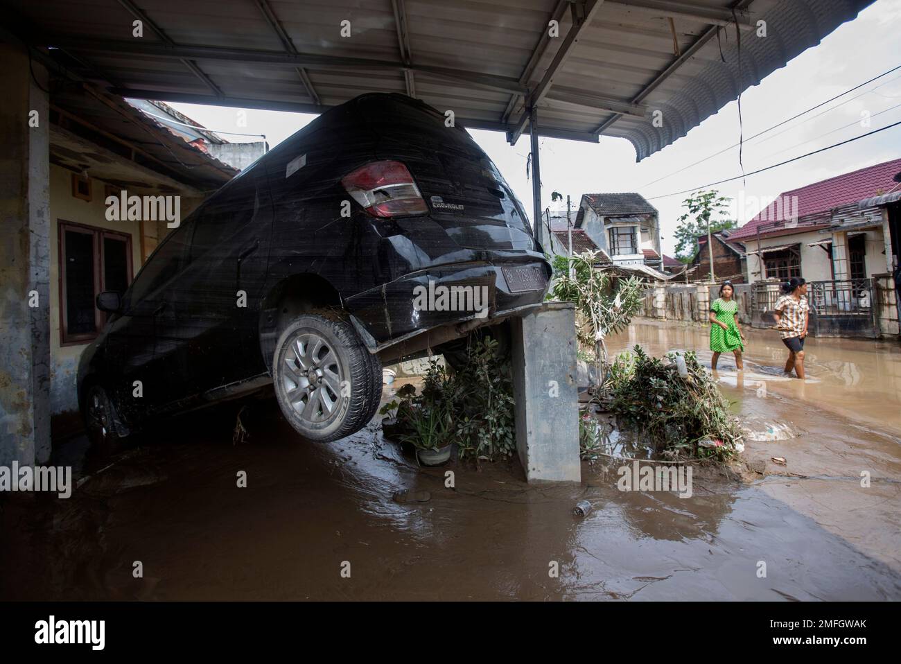 People walk past the wreckage of a car swept away by a flood at a ...
