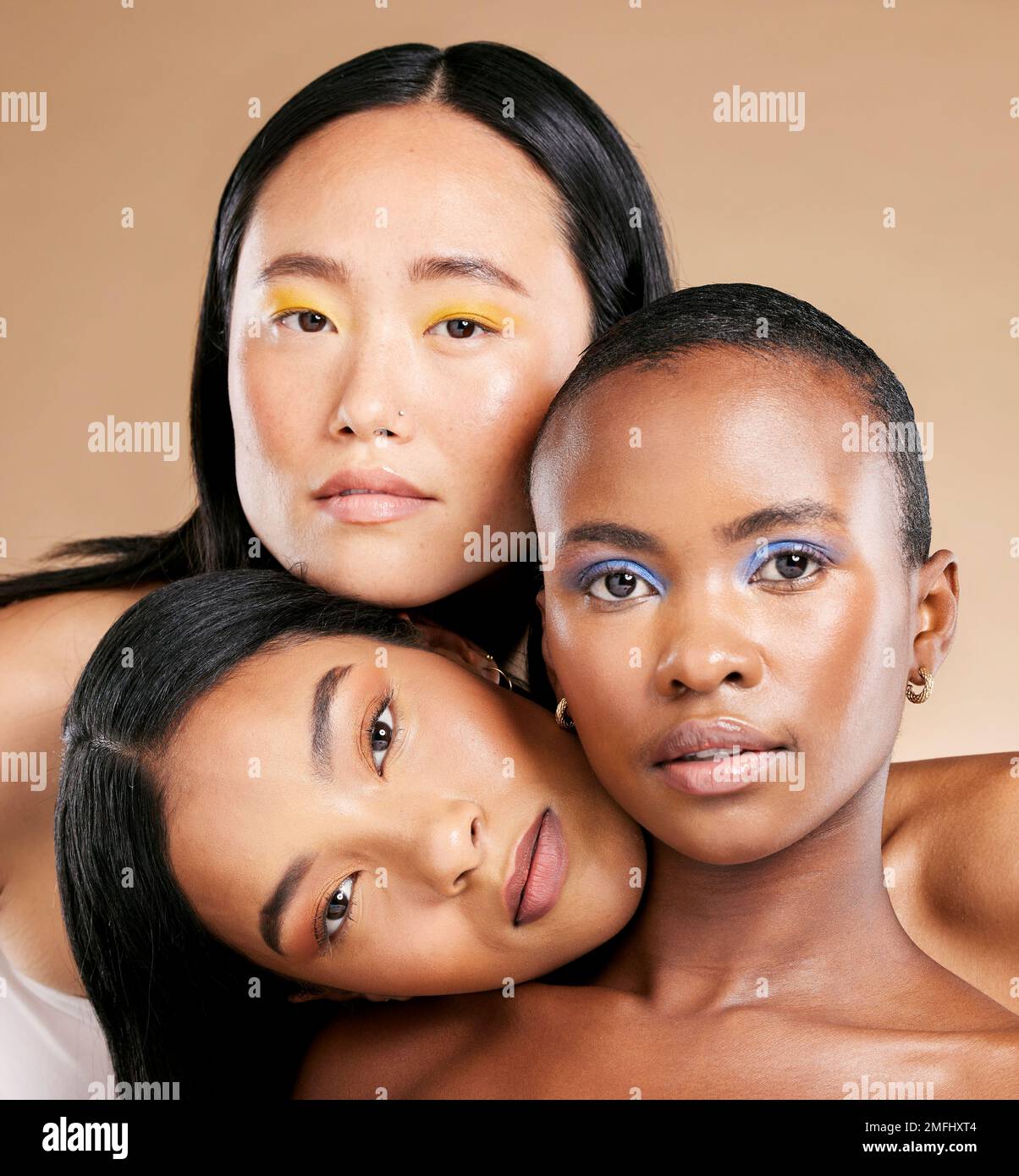Diversity, woman and focus face with makeup, skincare beauty and cosmetics dermatology in brown background studio. Interracial models, facial care and Stock Photo