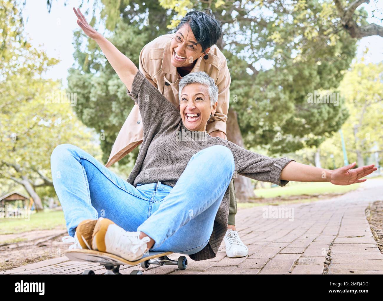 Senior women, park and couple of friends together outdoor for comic fun on a skateboard while happy. People together in nature for bonding, happiness Stock Photo