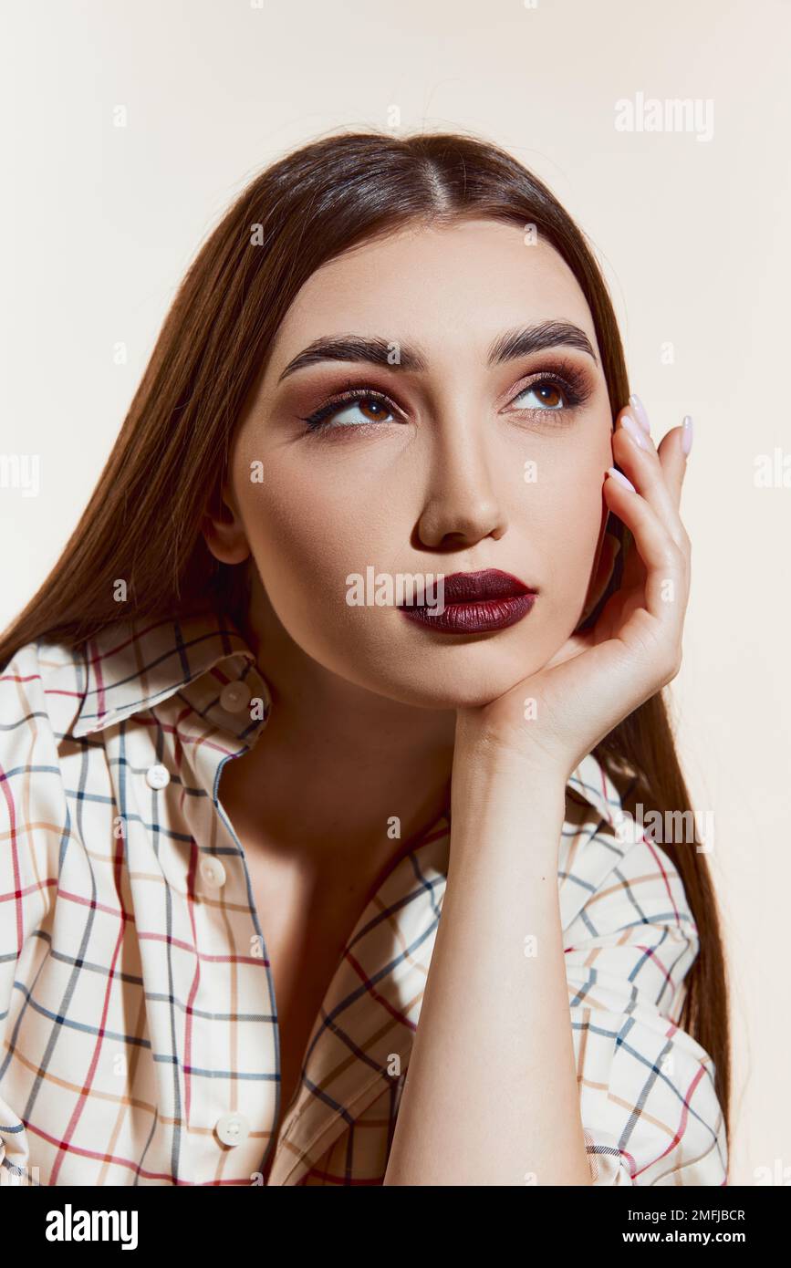 Portrait of young beautiful girl with straight brown hair, deep red lips makeup posing over white studio background. Concept of beauty, skincare Stock Photo