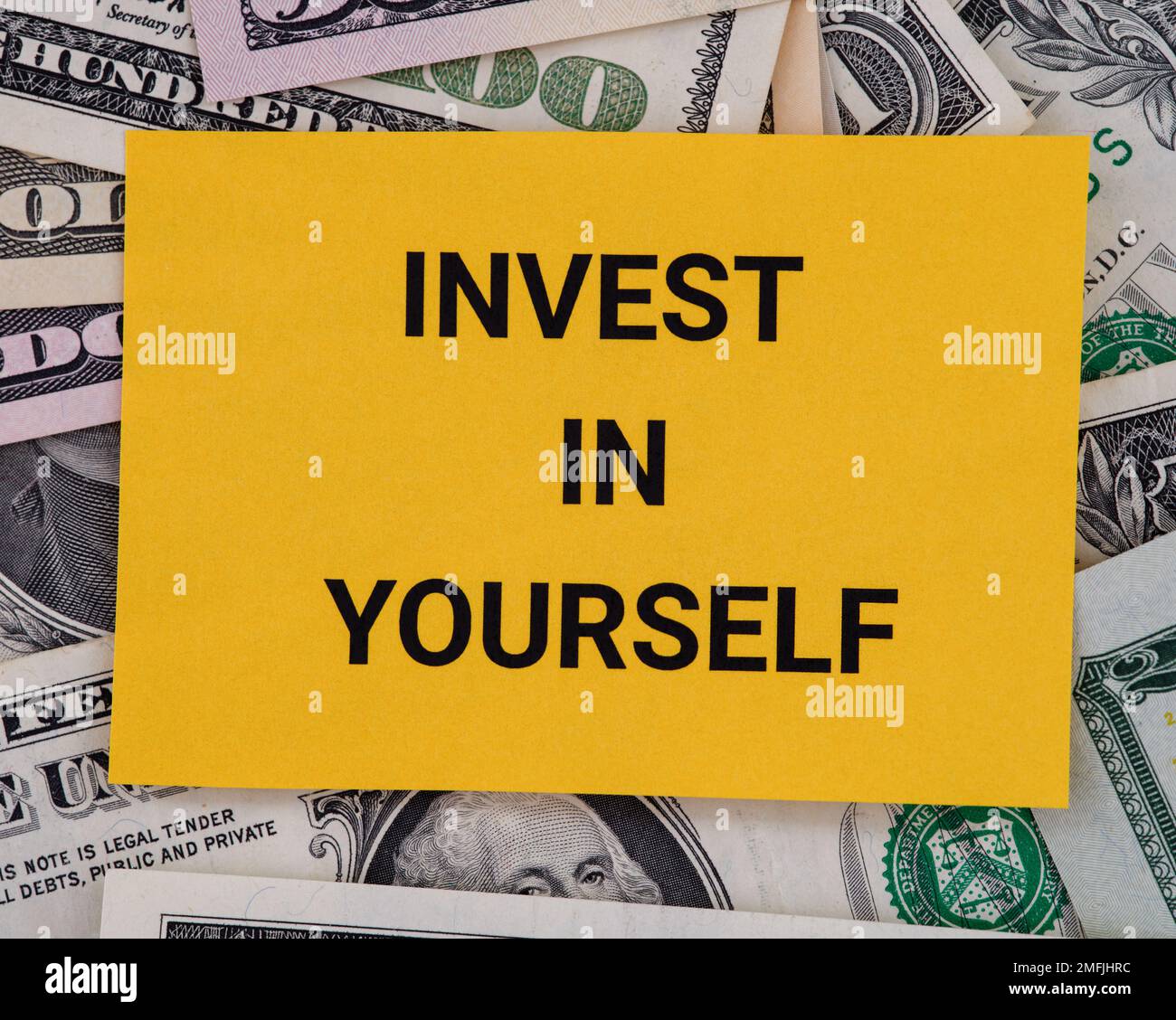 A yellow piece of paper with the phrase Invest in yourself lying on a pile of dollar bills. Close up. Stock Photo
