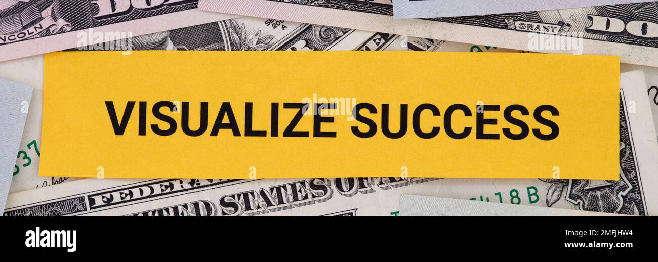 A yellow piece of paper with the phrase Visualize Success lying on a pile of dollar bills. Close up. Stock Photo