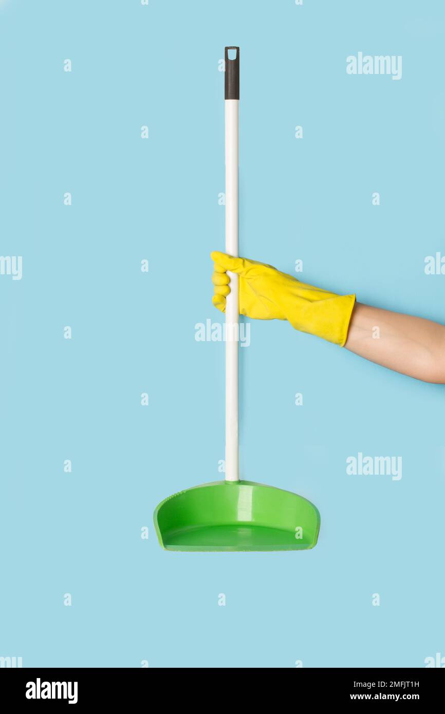 Woman with yellow rubber gloves holding a dustpan on a light blue