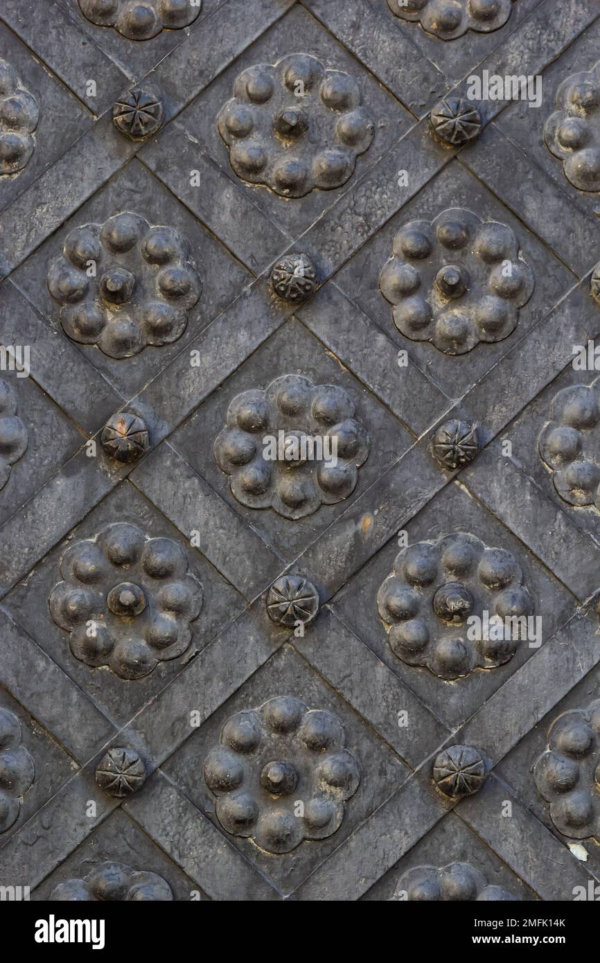An old metal door, forged gates, rivets on the facade of a cast-iron door, a round handle to open the door, the texture of old iron. High quality phot Stock Photo