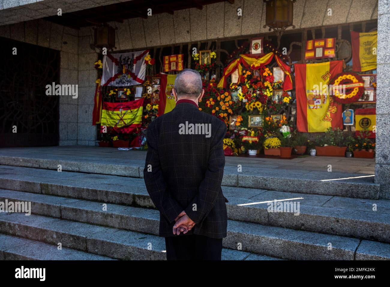 A man stands next to a shrine with flowers and Spanish flags marking