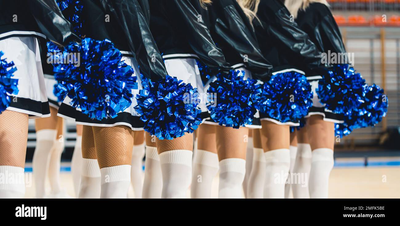 Blue pom-poms being held by the cheerleaders standing in line. Sports hall blurred in the background. High quality photo Stock Photo