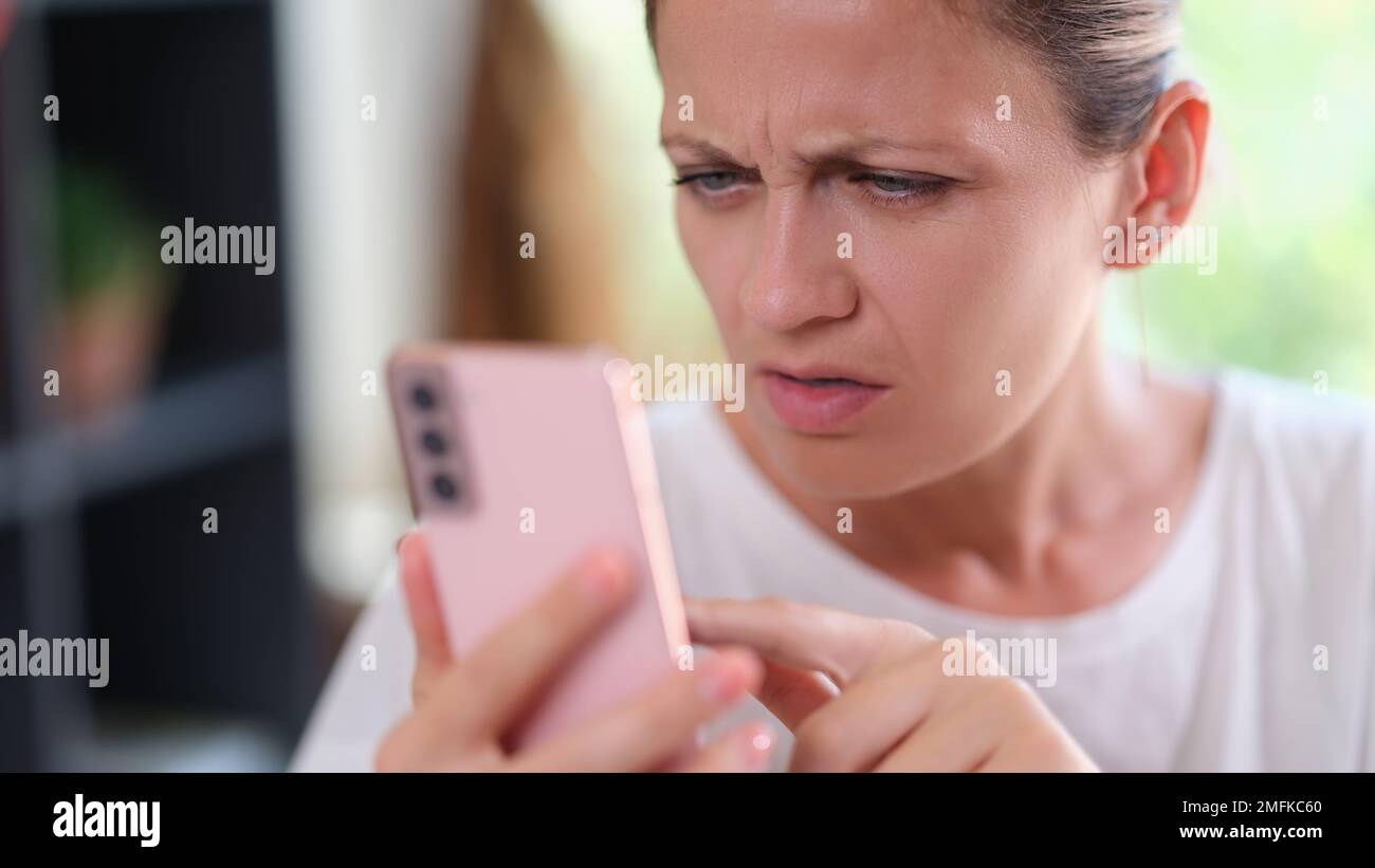 Woman with serious face looks doubtful at smartphone screen. . Stock Photo