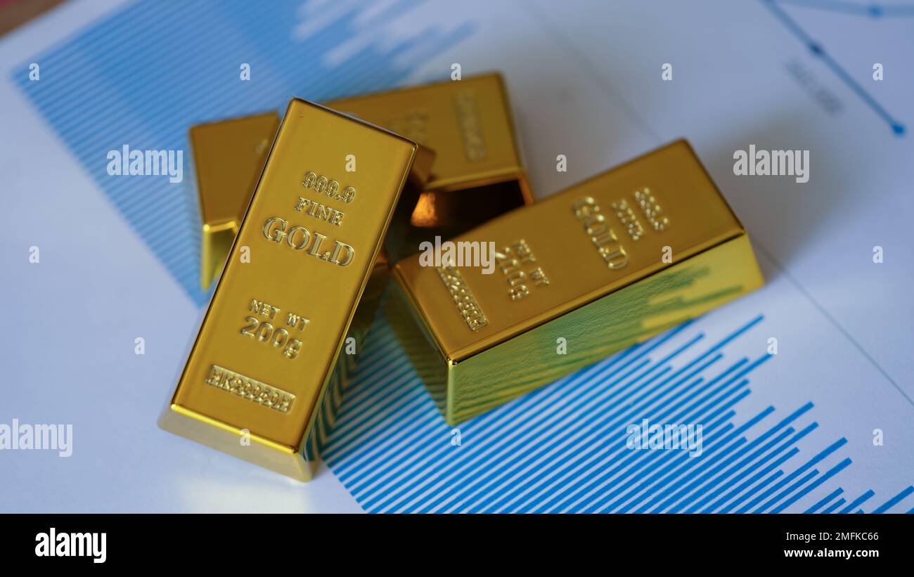 Gold bars on financial documents with charts and graphs closeup Stock