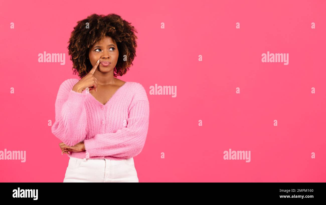 Pensive millennial african american curly woman in casual looking at empty space, thinking isolated on pink background Stock Photo