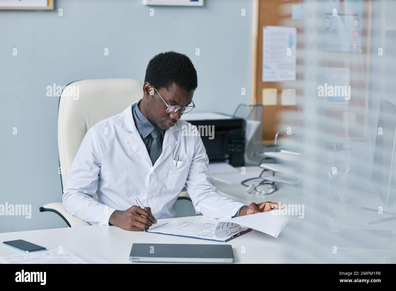 Portrait of young black doctor filling papers at desk in office while working in private clinic Stock Photo