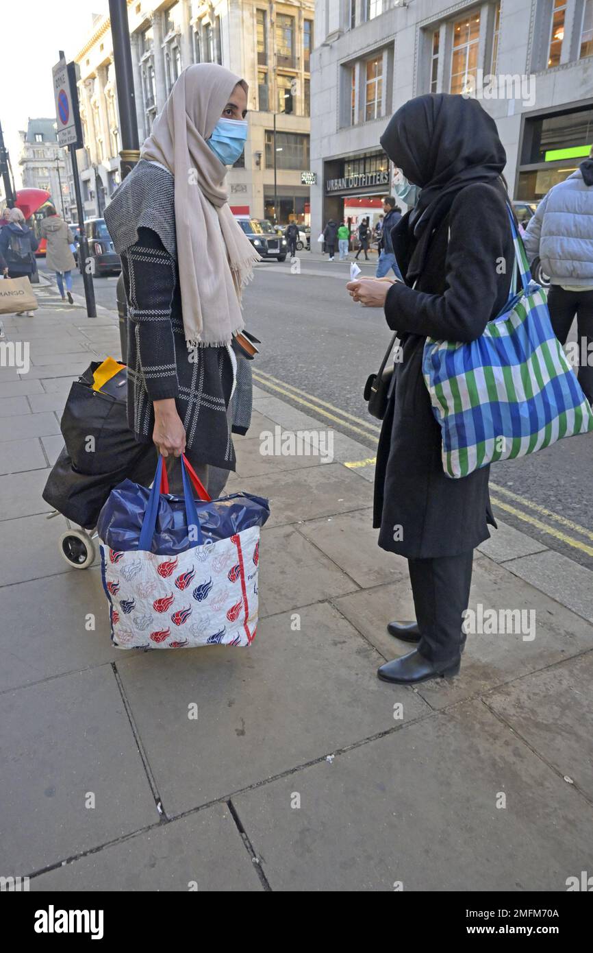 London, England, UK. Two muslim women wearing headscarves and facemasks talking in Oxford Street. Jan 2023 Stock Photo