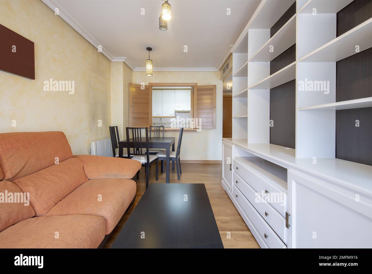 Small living room with motley furniture occupying the space, a square dining table next to a hatch window to the kitchen Stock Photo