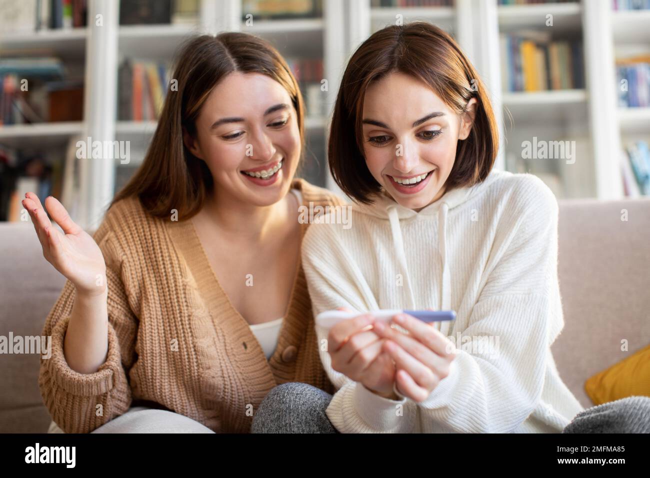 Glad surprised amazed pretty european millennial women with pregnancy test rejoice positive result Stock Photo
