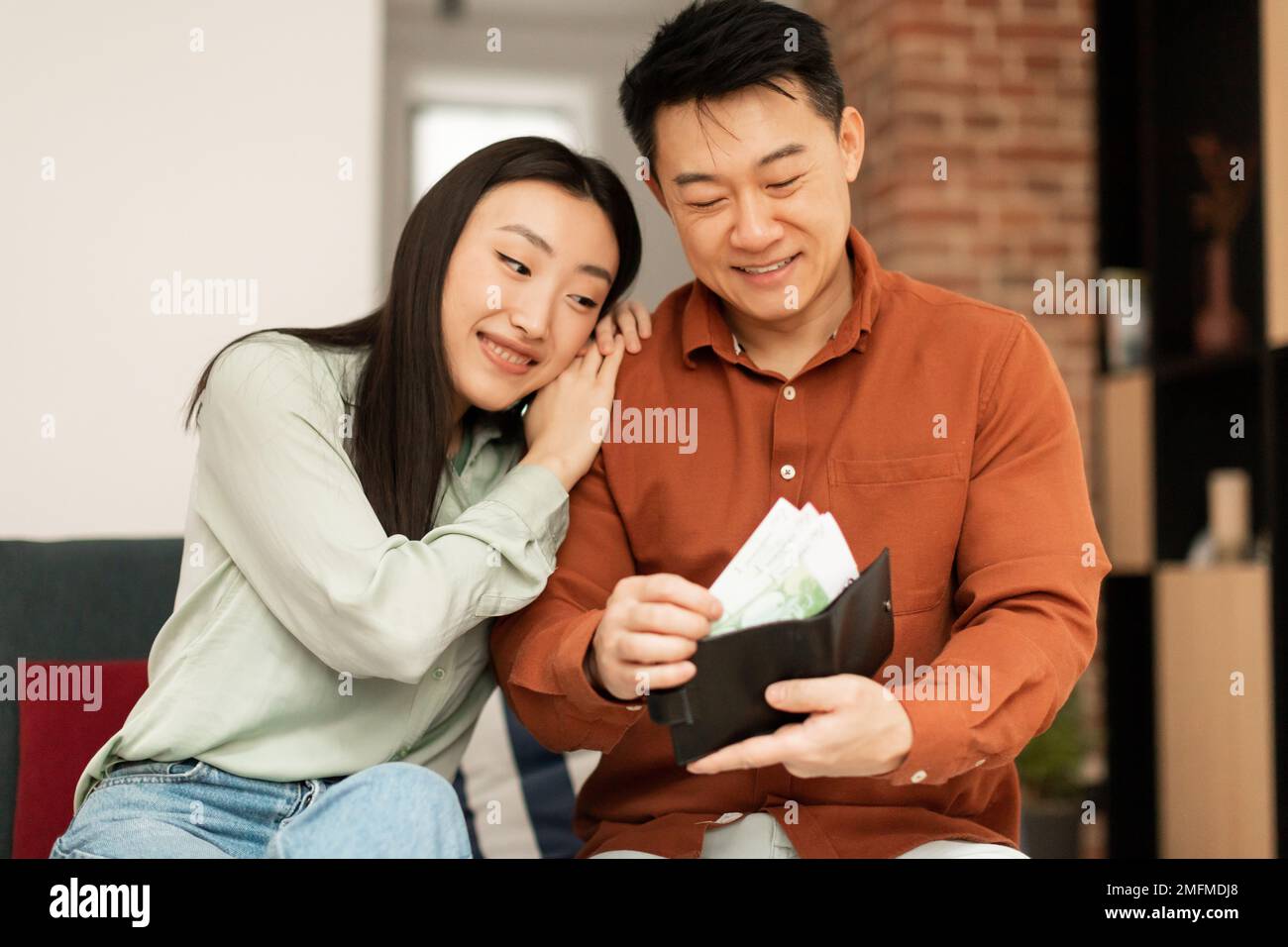Finance and money saving concept. Happy asian man putting banknotes