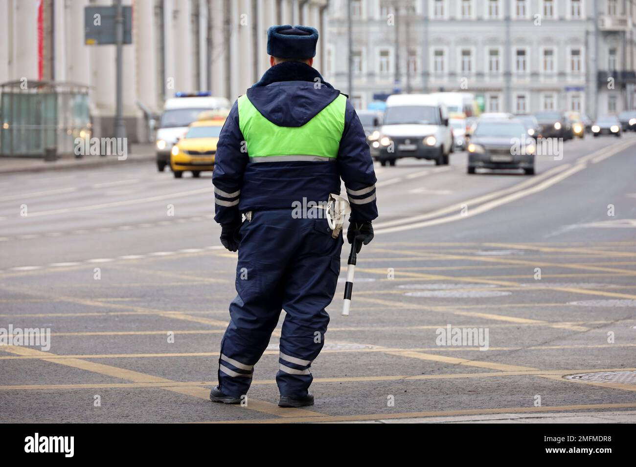 Traffic police officer standing with rod on a road on cars background. Policeman patrol the city street Stock Photo