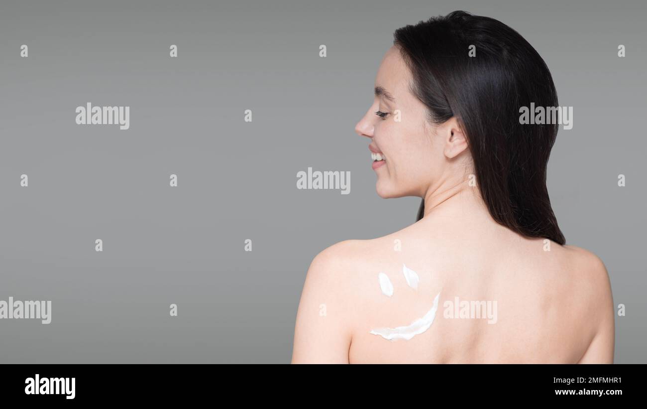 Cheerful young european naked female has cream smiley on skin, enjoy procedure, isolated on gray background Stock Photo