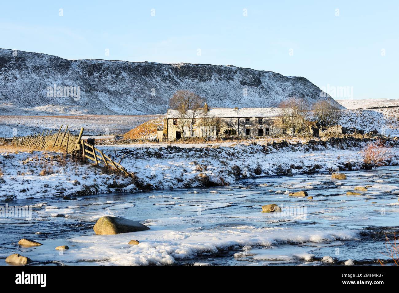 The imposing crags of Cronkley Fell and the old farmstead of Wheysike House viewed across Harwood Beck from the Pennine Way in winter, Forest-in-Teesd Stock Photo