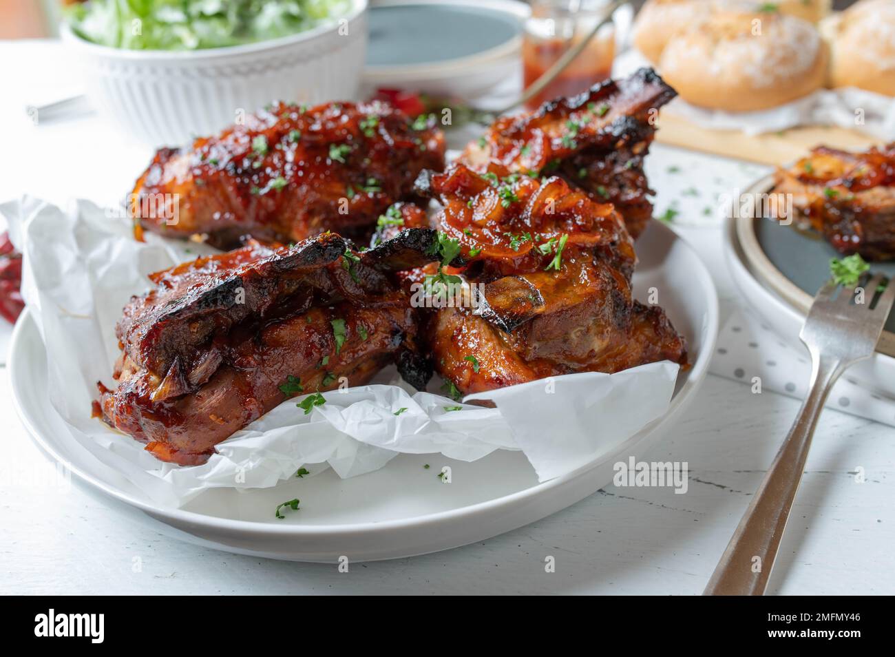Oven baked thick pork ribs with homemade barbecue sauce, salad and bread for dinner or lunch on a table Stock Photo