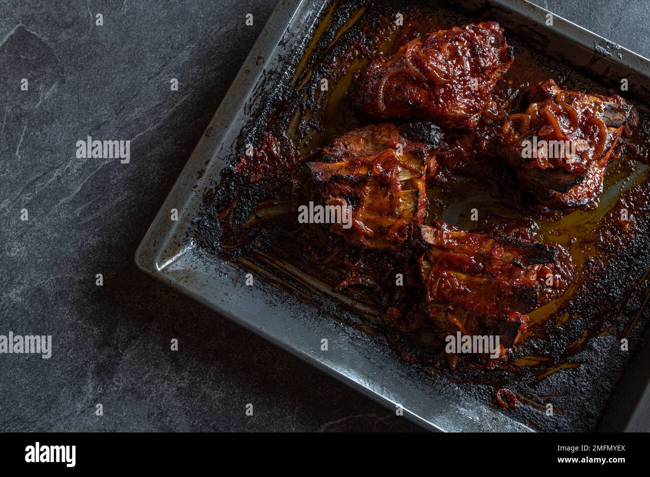 Thick pork ribs with homemade barbecue sauce on a baking tray isolated on dark background. Flat lay Stock Photo