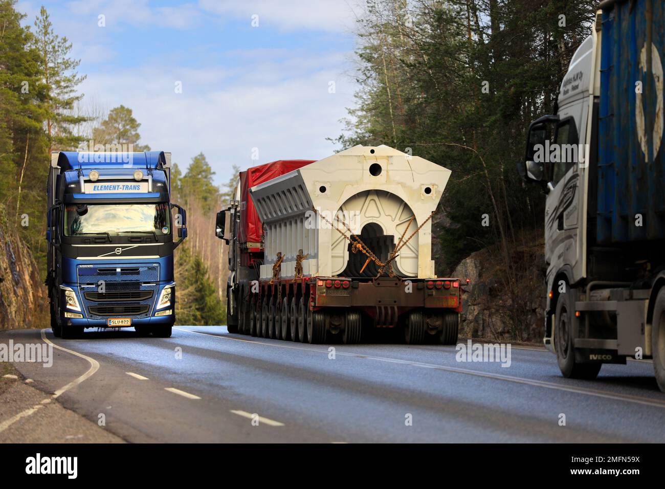 Freight transport trucks on highway with blue Volvo FH semi trailer and oversize load transport, rear view. Salo, Finland. January 20, 2023. Stock Photo