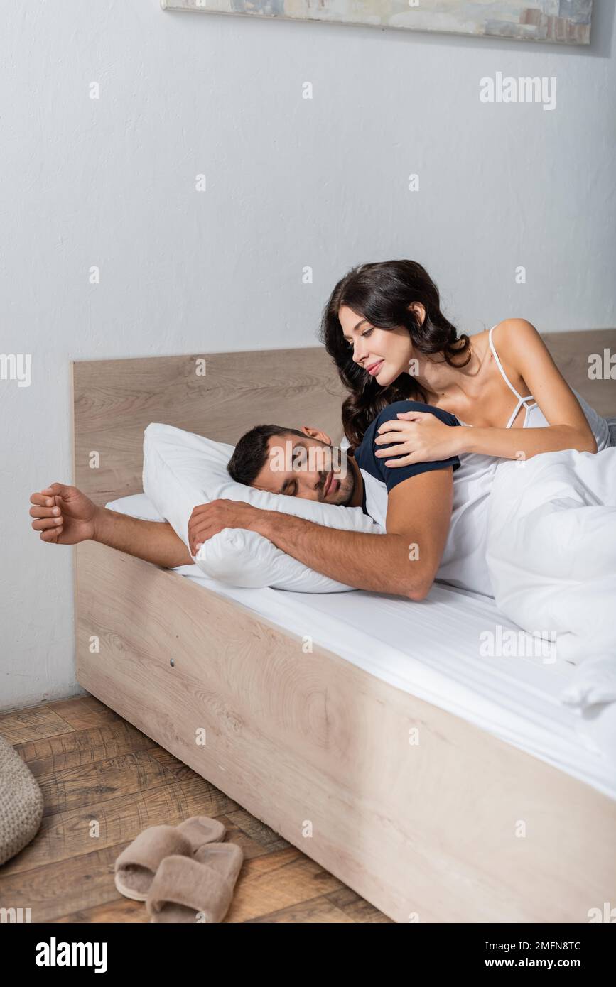 Smiling woman touching sleeping boyfriend on bed,stock image Stock Photo