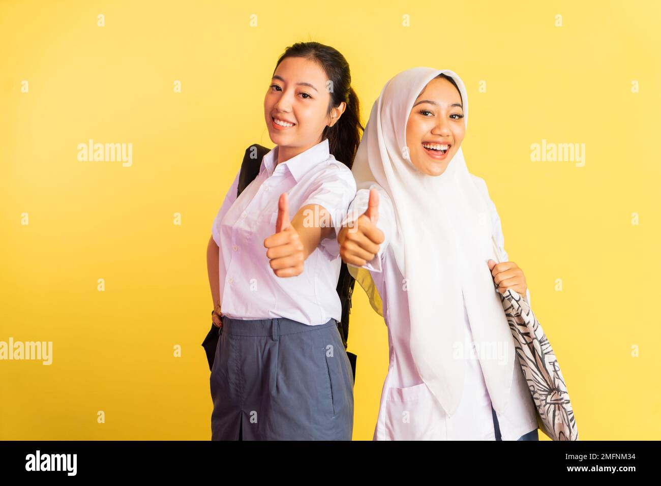 two high school girls standing carrying bags with thumbs up Stock Photo ...