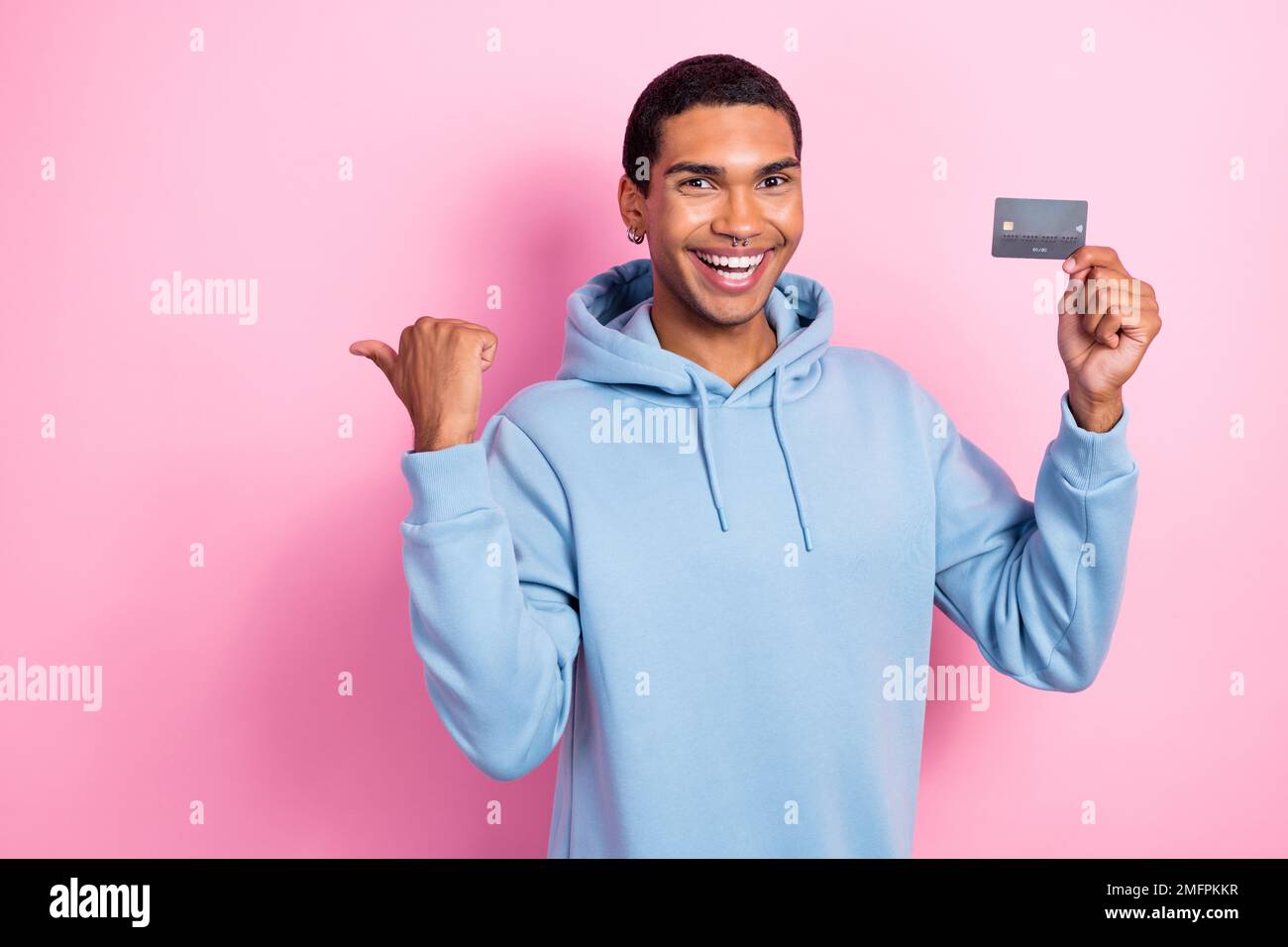 Photo of young excited man wearing blue sweatshirt direct finger empty space hold wireless new premium card isolated on pink color background Stock Photo