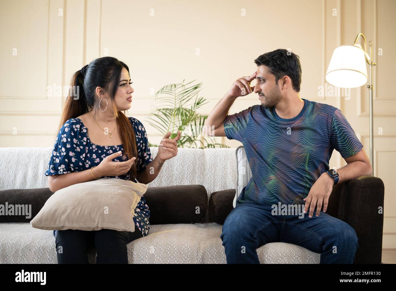 Angry indian couple fighting by shouting and arguing eachother while sitting on sofa at home - concept of break up, divorce and family problems Stock Photo