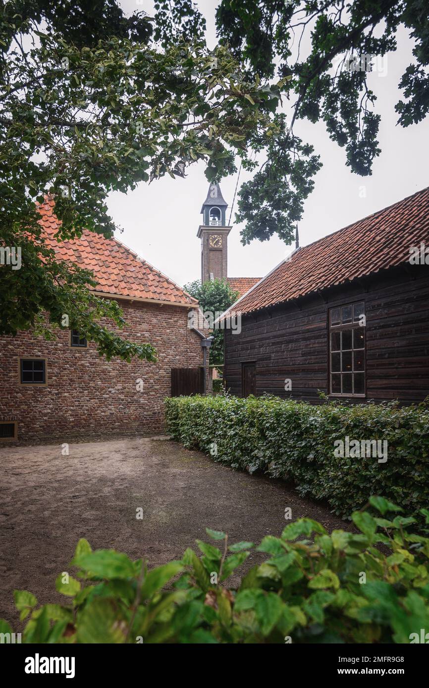 Empty courtyard between old houses overlooking the old church tower and surrounded by tree branches. Stock Photo